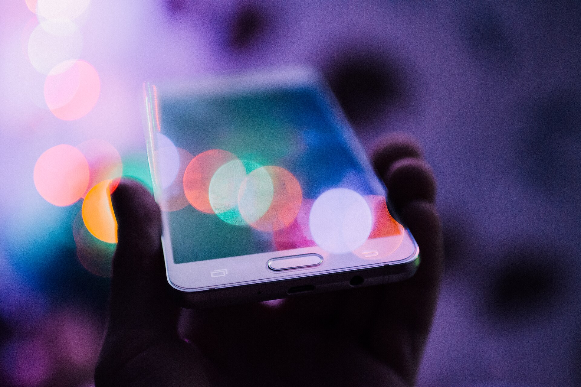 Hand holding a smartphone against blurred colorful lights, illustrating a cloud account tip and AI-generated images investigation