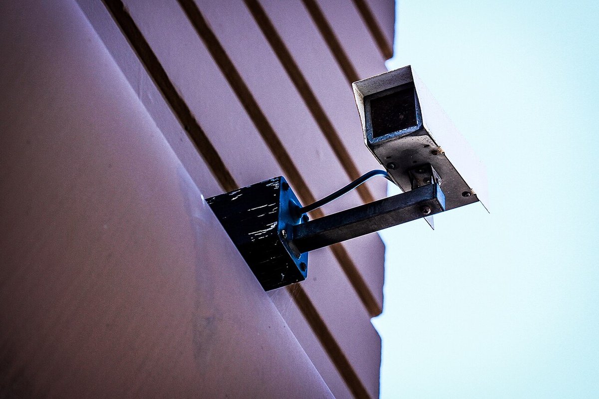 Security camera mounted on the side of a building against a pale sky